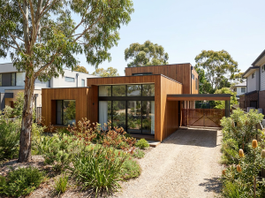 Modern prefabricated home exterior in an Australian suburban setting with timber cladding and native garden landscaping